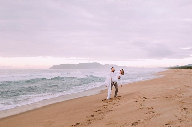 Pré Wedding de Bianca e Raul na Praia de Moçambique Florianópolis em um dia ensolarado, Noiva de vestido casual branco com Penteado de Pré Wedding e Maquiagem de Pré Wedding by Fernanda Dresch 